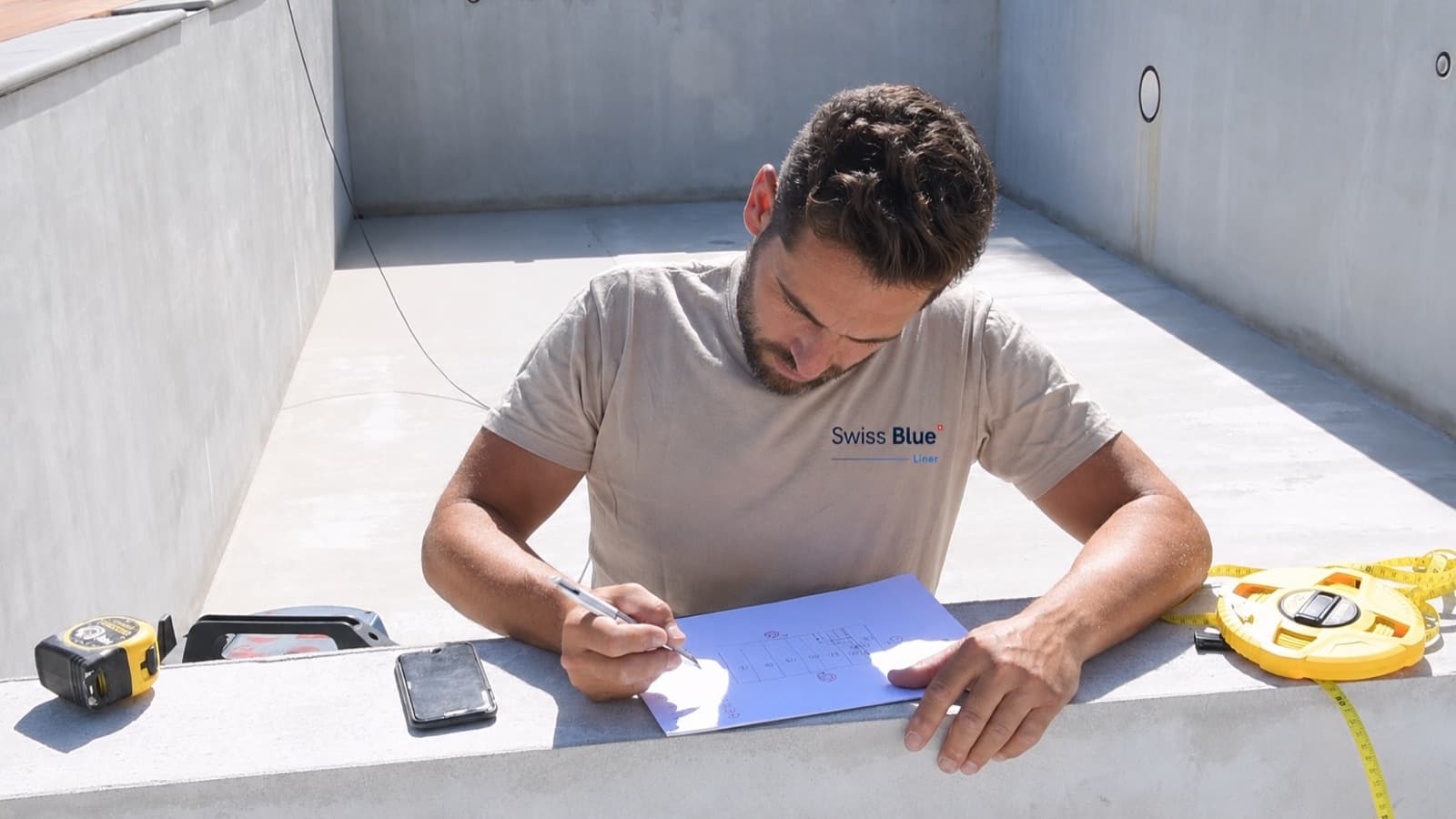 Le responsable Swissblue Liner relève les cotes d’un bassin en béton, plan à la main, avant la pose du liner armé